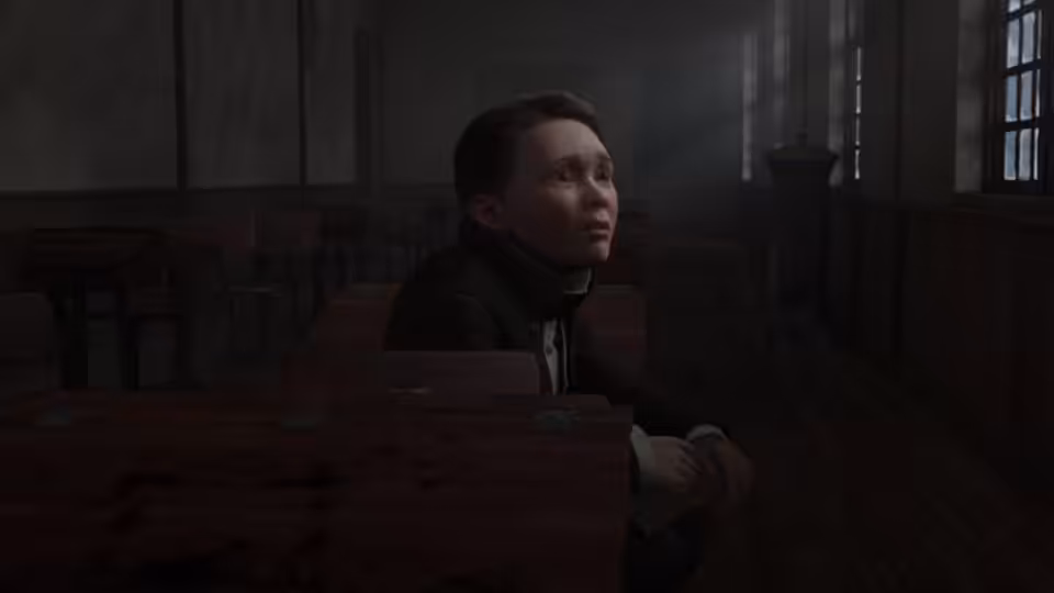 A boy sits alone at a desk in a dim classroom