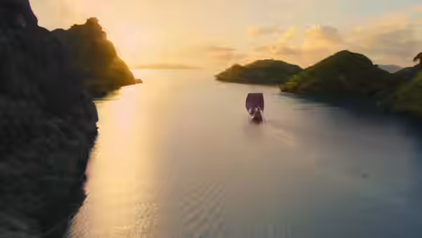 The Dawn Treader sails between rocky islands across a calm bay at sunset