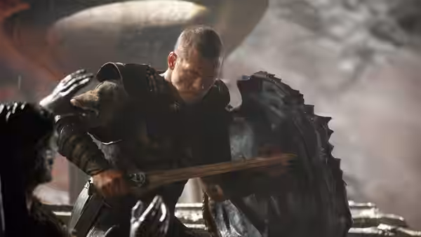 Perseus (Sam Worthington) crouches behind a shield, gripping his sword amid battle