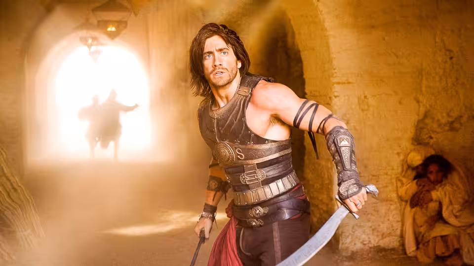 Prince Dastan (Jake Gyllenhaal) holds a sword in a sandstone passage as a figure approaches