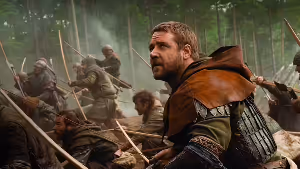 Robin Longstride (Russell Crowe) crouches among armed men fighting in a forest