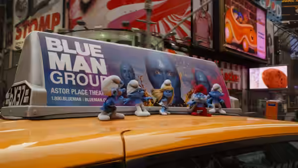 Several Smurfs stand on a taxi beneath a Blue Man Group advertisement