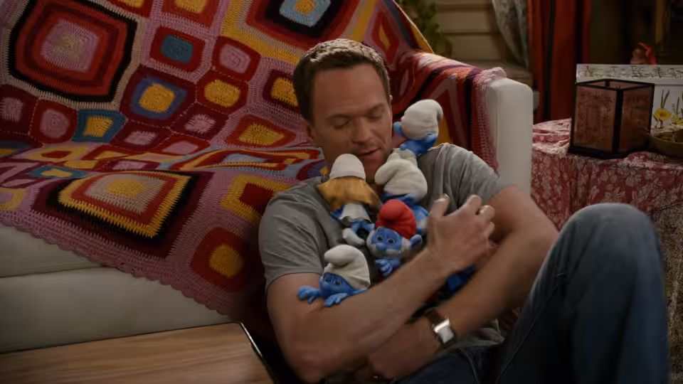 Patrick Winslow (Neil Patrick Harris) cuddles a bundle of Smurfs on a sofa