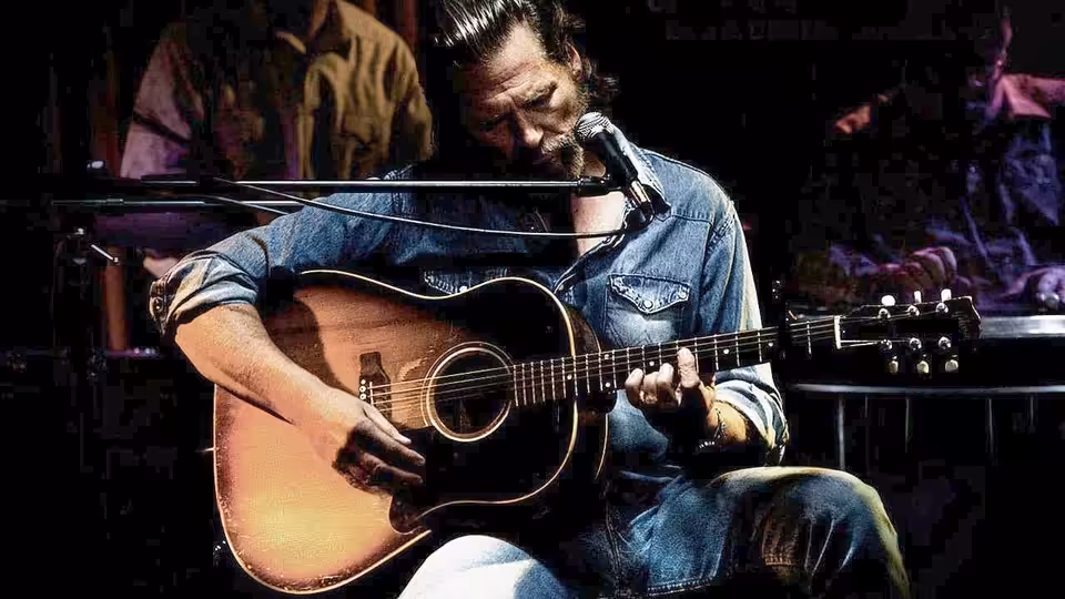 Bad Blake (Jeff Bridges) sings into a microphone while playing acoustic guitar onstage