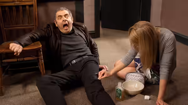 A woman kneels beside Johnny English (Rowan Atkinson), who lies on the floor in alarm