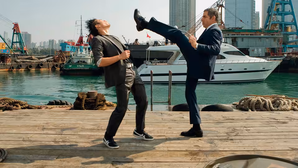 Johnny English (Rowan Atkinson) kicks a man on a wooden dock beside a yacht