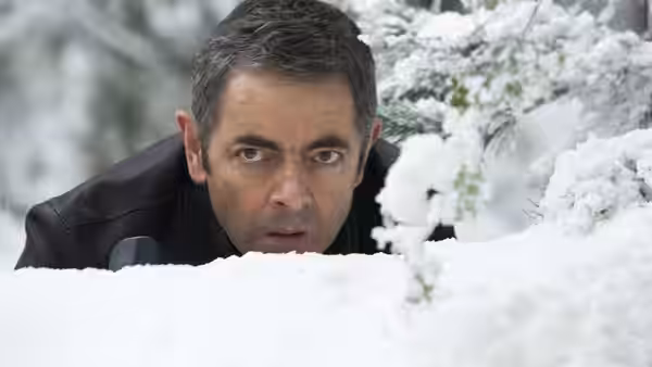 Johnny English (Rowan Atkinson) peers over a snowbank among snow-covered branches
