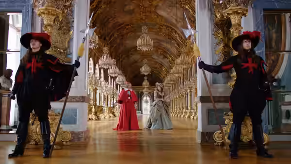 Guards hold the doors of an ornate palace hall as two women approach