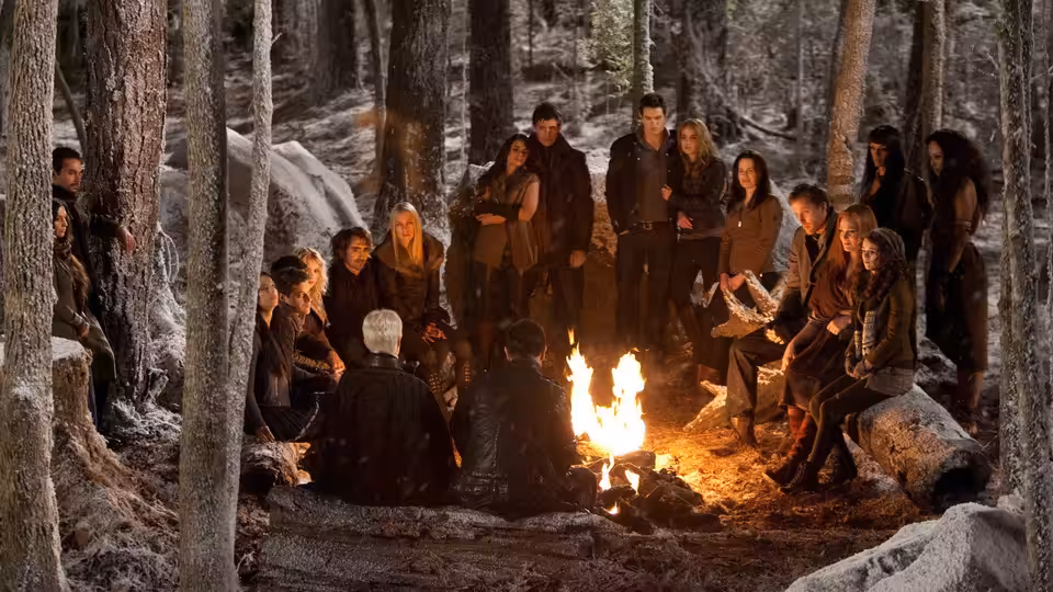A group of vampires gathers around a campfire among snow-dusted trees