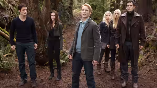 Edward Cullen, Bella Swan, and other vampires stand among trees in a forest