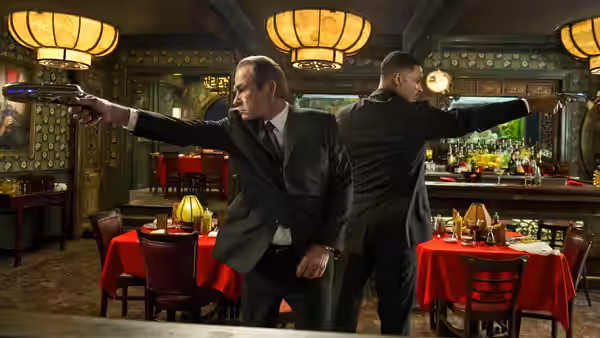 Agent K (Tommy Lee Jones) and Agent J (Will Smith) aim weapons in a red-lit restaurant