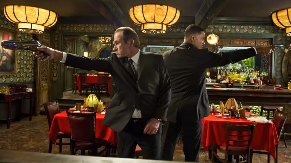 Agent K (Tommy Lee Jones) and Agent J (Will Smith) aim weapons in a red-lit restaurant