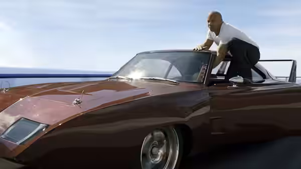 Luke Hobbs (Dwayne Johnson) climbs onto a classic car beside the water