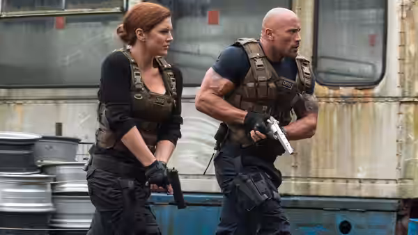 Luke Hobbs (Dwayne Johnson) and an armed woman move beside a metal trailer
