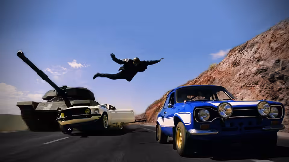 A person dives above a mountain road as a blue car, a white car and a tank race past