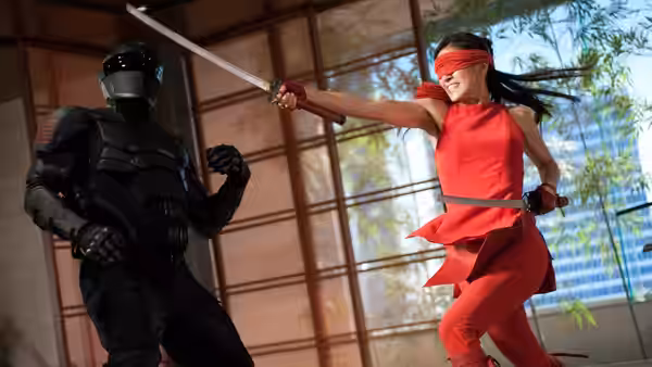 Jinx (Élodie Yung) swings a sword at an armored opponent inside a glass-walled dojo