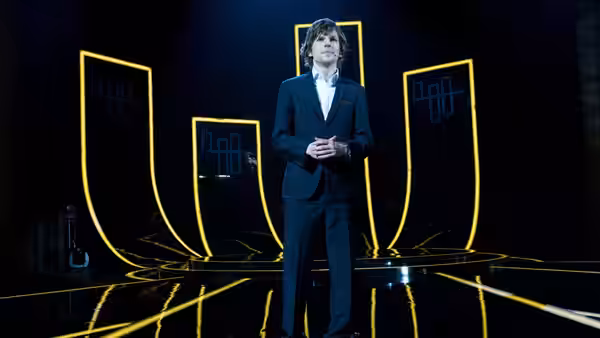 J. Daniel Atlas (Jesse Eisenberg) stands on a stage framed by glowing yellow panels