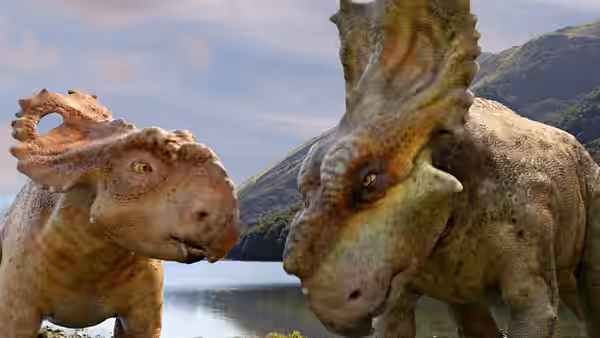 Two horned dinosaurs face each other beside a mountain lake