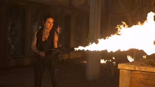 Clary Fray (Lily Collins) holds a weapon as flames burst across a dim room