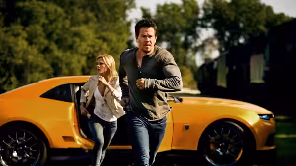 Cade Yeager (Mark Wahlberg) runs past a yellow sports car as Tessa follows
