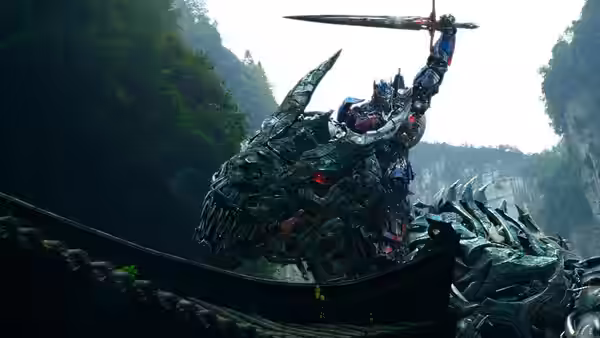 Optimus Prime raises a sword while riding a spiked mechanical creature through a ravine