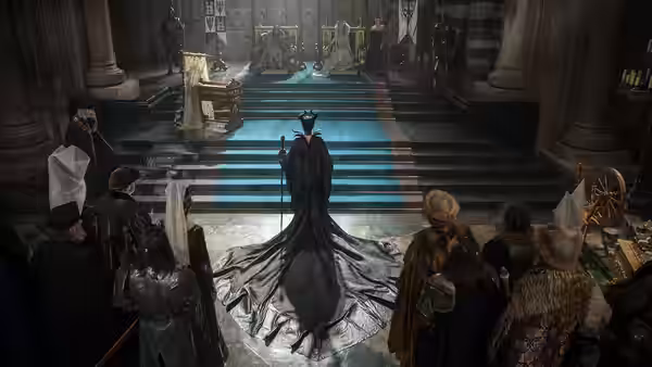 Maleficent (Angelina Jolie) enters a castle hall as courtiers gather around the stairs