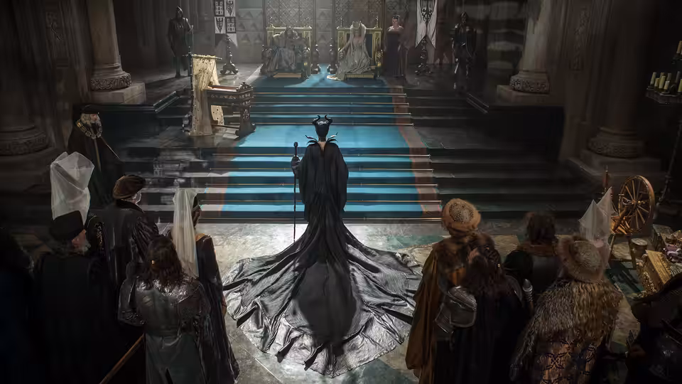 Maleficent (Angelina Jolie) enters a castle hall as courtiers gather around the stairs