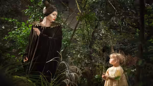 Maleficent (Angelina Jolie) watches young Aurora in a forest clearing