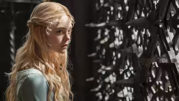 Aurora (Elle Fanning) studies a spiked wooden barrier inside a stone room