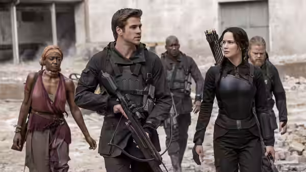 Katniss Everdeen (Jennifer Lawrence) and Gale Hawthorne (Liam Hemsworth) walk armed through the ruins