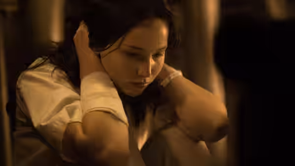 Katniss Everdeen (Jennifer Lawrence) covers her ears in a dimly lit room