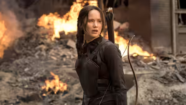 Katniss Everdeen (Jennifer Lawrence) turns amid burning rubble, bow and arrows on her back
