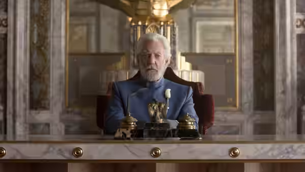 President Snow (Donald Sutherland) sits behind a desk in an ornate room