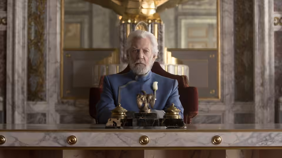 President Snow (Donald Sutherland) sits behind a desk in an ornate room