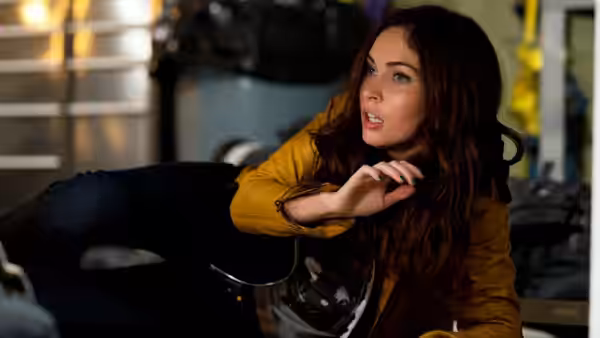 April O'Neil (Megan Fox) crouches and looks alert inside a room
