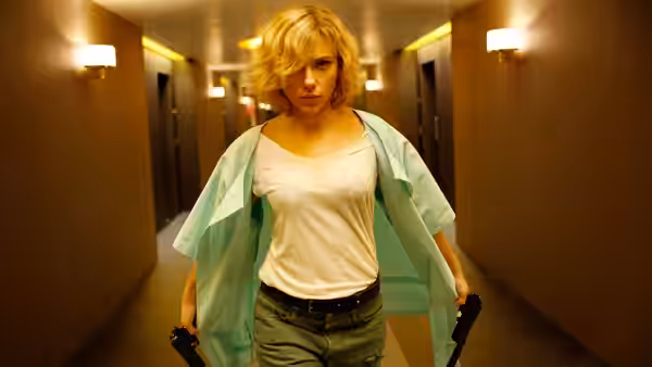 Lucy (Scarlett Johansson) walks down a hotel corridor carrying guns