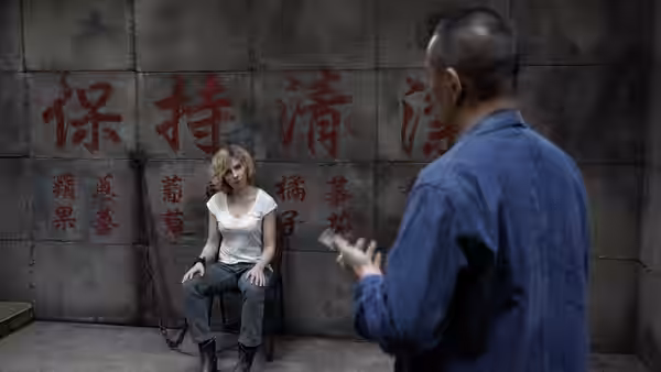 Lucy (Scarlett Johansson) sits against a wall covered in Chinese writing as a man faces her