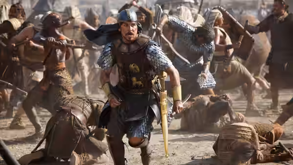 An armored soldier runs through a battlefield as fighters clash and fall around him