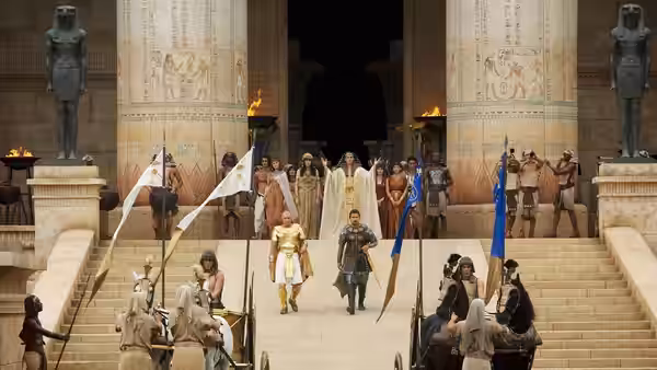 Moses (Christian Bale) and Ramses (Joel Edgerton) descend palace steps amid soldiers and attendants