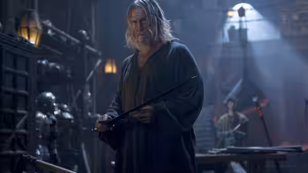 Master John Gregory (Jeff Bridges) holds a weapon in an armory as Tom watches behind him