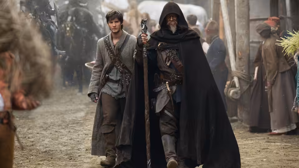 Tom Ward (Ben Barnes) walks through a crowded village beside Master John Gregory (Jeff Bridges)