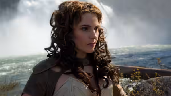Alice Deane (Alicia Vikander) stands by the water in a wooded landscape