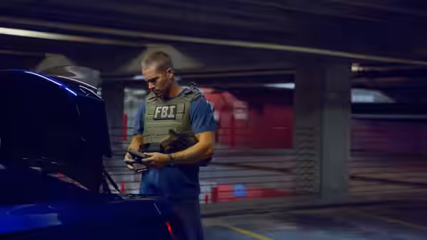 Brian O'Conner (Paul Walker), wearing an FBI vest, examines a device beside an open car