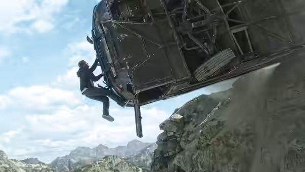 A man clings to the underside of an aircraft above a rocky mountain slope
