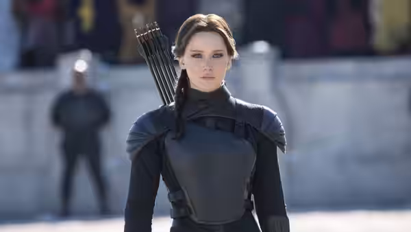 Katniss Everdeen (Jennifer Lawrence), wearing combat armor and carrying arrows, stands before a blurred crowd