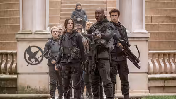 Katniss Everdeen (Jennifer Lawrence) and armed fighters advance outside a building marked with a mockingjay