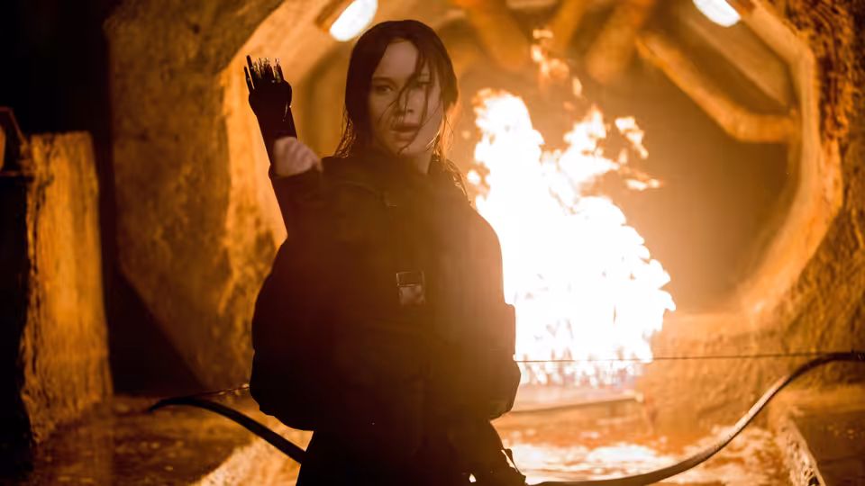 Katniss Everdeen (Jennifer Lawrence) raises a hand before flames in a dark tunnel