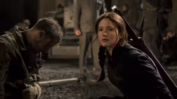 Katniss Everdeen (Jennifer Lawrence) crouches beside a wounded man in a rubble-strewn street