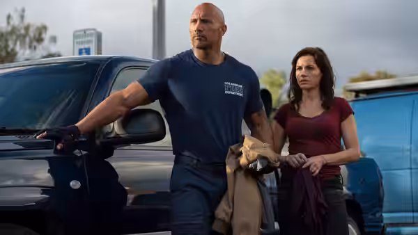 Ray Gaines (Dwayne Johnson) stands beside a vehicle holding a jacket as Emma Gaines (Carla Gugino) looks on