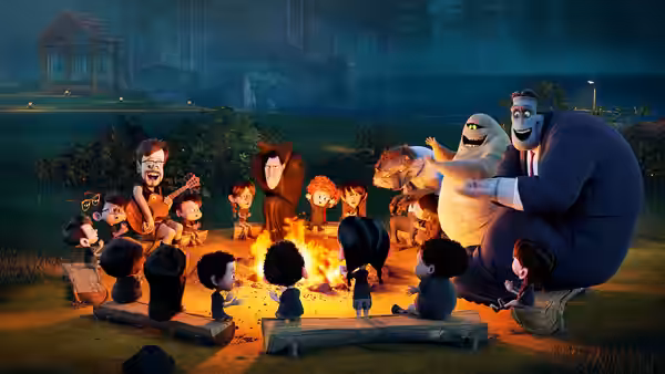 Frankenstein and a group of monsters gather around a campfire outdoors